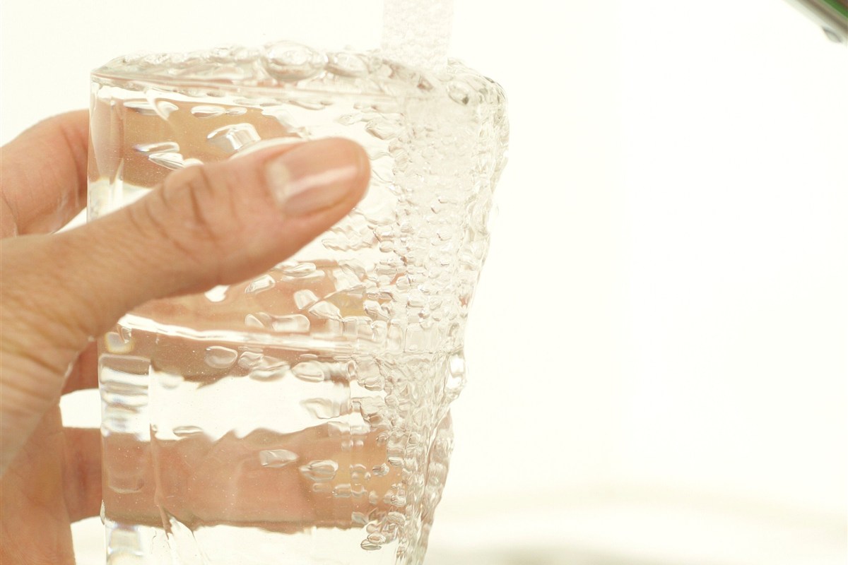 A hand holds a clear glass of water beneath a kitchen tap.