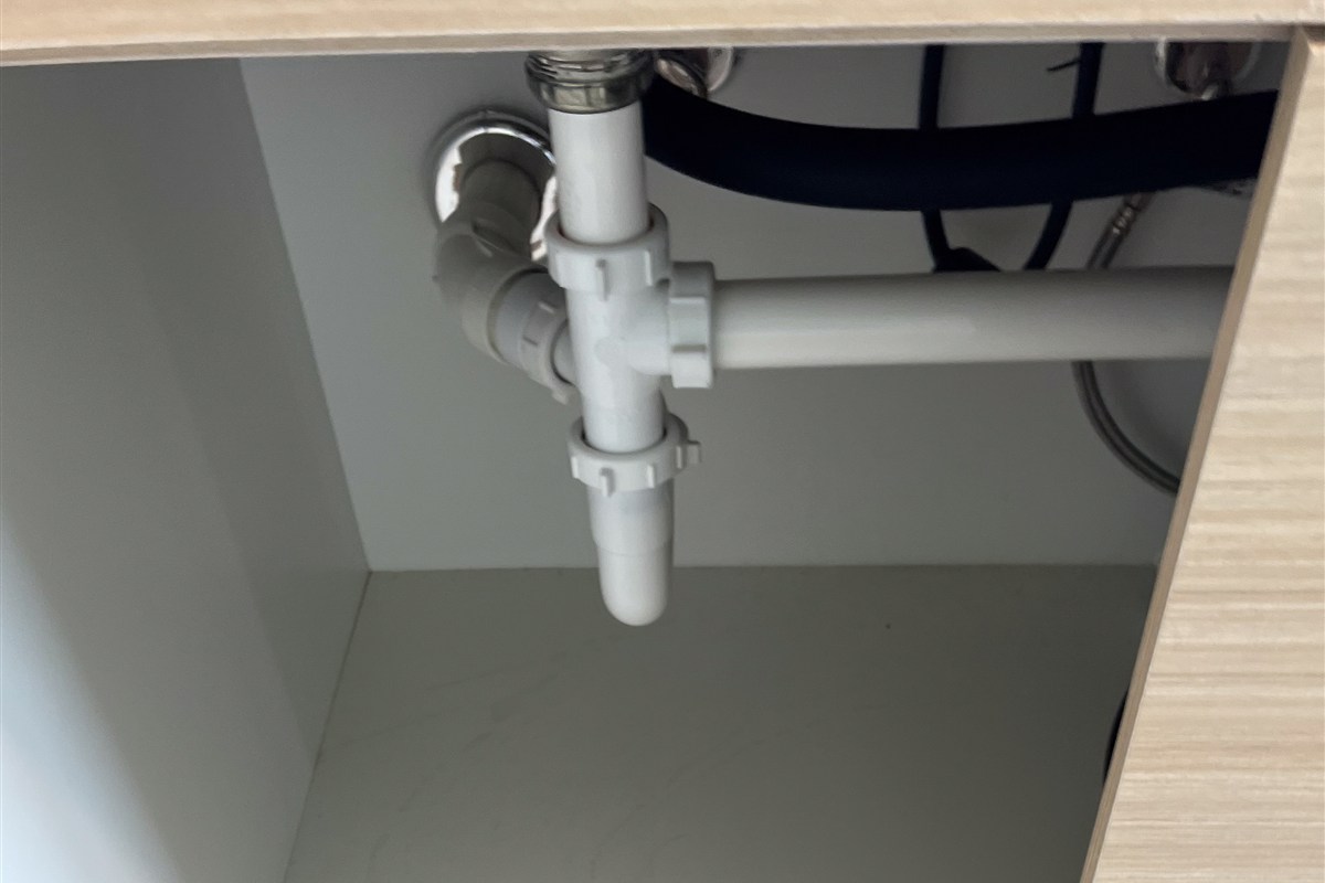 White drain pipes inside a kitchen sink cabinet.
