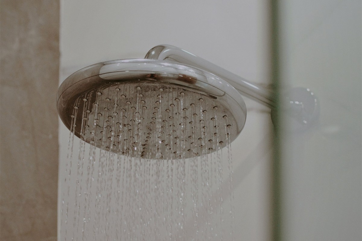 Water flowing from a chrome showerhead in a tiled bathroom.