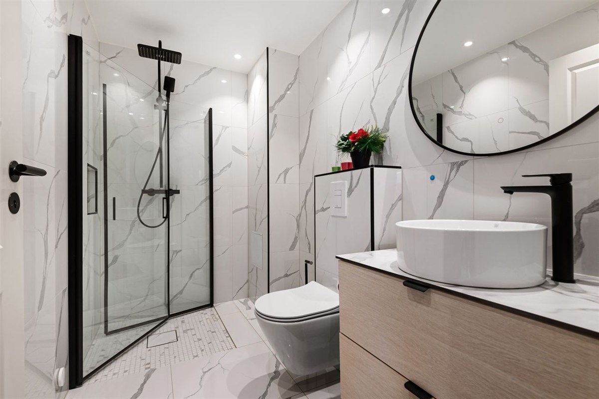 Bathroom shower and sink with black fixtures against marble-patterned walls.